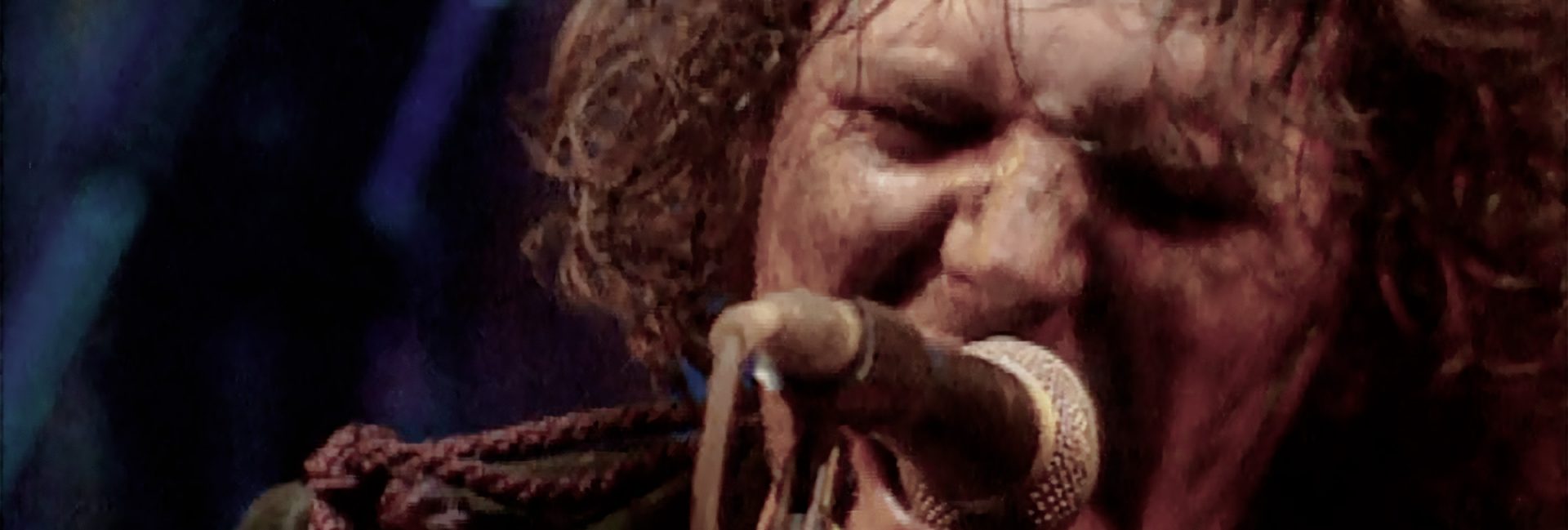 Close up photo of Tim Smith of Cardiacs from live video, singing on microphone