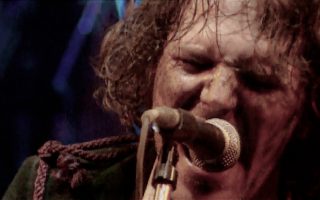 Close up photo of Tim Smith of Cardiacs from live video, singing on microphone