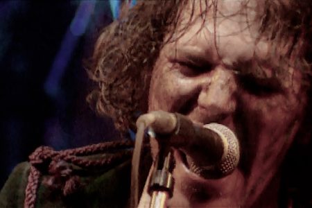 Close up photo of Tim Smith of Cardiacs from live video, singing on microphone